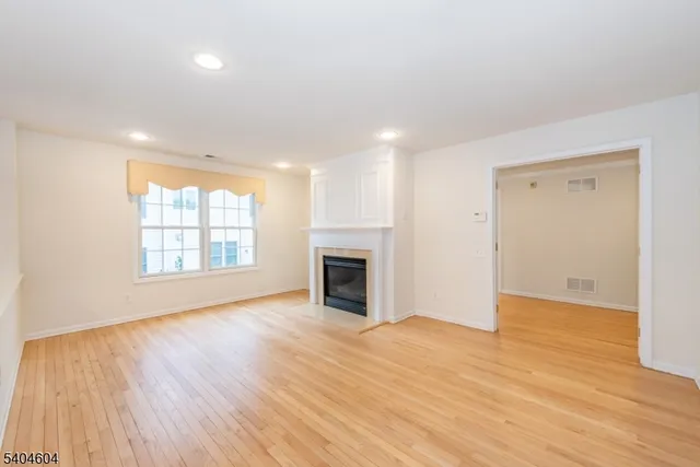 an empty room with wooden floor fireplace and windows