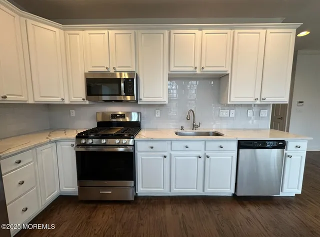 a kitchen with stainless steel appliances granite countertop a stove a sink and white cabinets