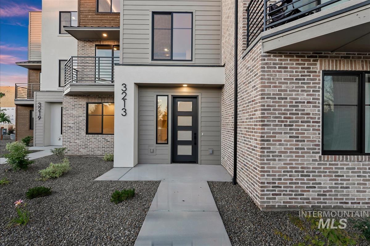 3213 West Moore Street Boise, ID 83702 - Photo 2 of 32 Contemporary multi-level residence featuring a modern dark-paneled entry door, contrasting light brick and horizontal siding, black-framed windows, and an upper-level balcony with metal railings
