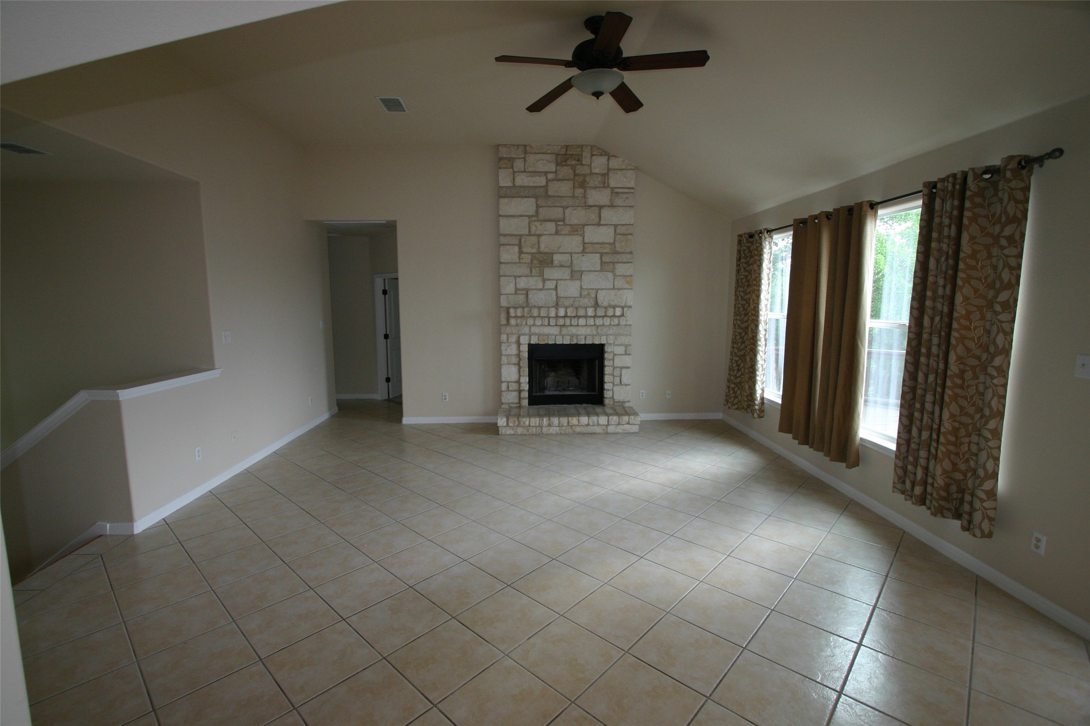 Unfurnished living room with ceiling fan, light tile patterned floors, a stone fireplace, and vaulted ceiling