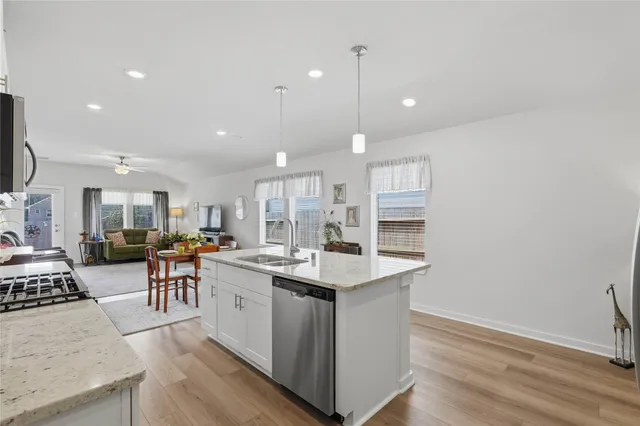 a kitchen with stainless steel appliances granite countertop a stove oven a sink dishwasher and a dining table with wooden floor