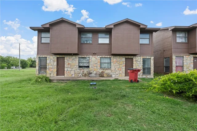 a brick house that has a small yard and a large tree
