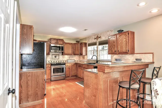 a kitchen with stainless steel appliances granite countertop a stove top oven a sink dishwasher and a refrigerator with wooden cabinets