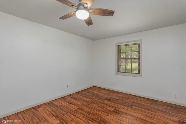 an empty room with wooden floor fan and windows