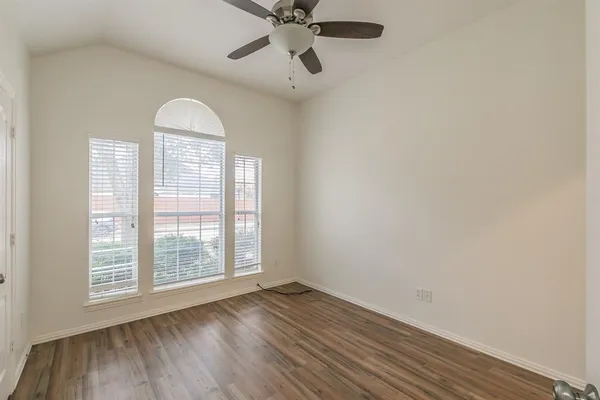 an empty room with wooden floor fan and windows