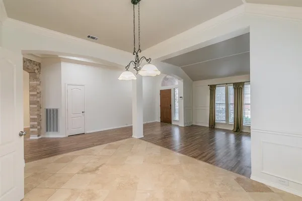 a view of an empty room with wooden floor and a chandelier