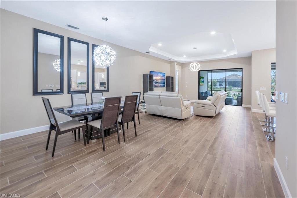 8448 Rosa Court Naples, FL 34114 - Photo 3 of 24 Open-concept interior featuring wood-finish flooring, a tray ceiling with recessed lighting, and a modern dining area with a statement chandelier