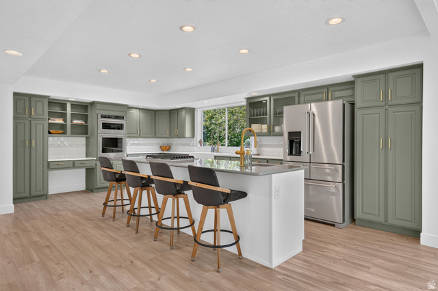 1979 Cave Hollow Way Bountiful, UT 84010 - Photo 11 of 59 Spacious kitchen featuring sage green cabinetry, stainless steel appliances, a large center island with counter seating, and wood-finish flooring