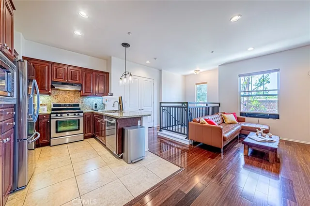 a kitchen with stainless steel appliances kitchen island granite countertop a refrigerator stove top oven and couches with wooden floor