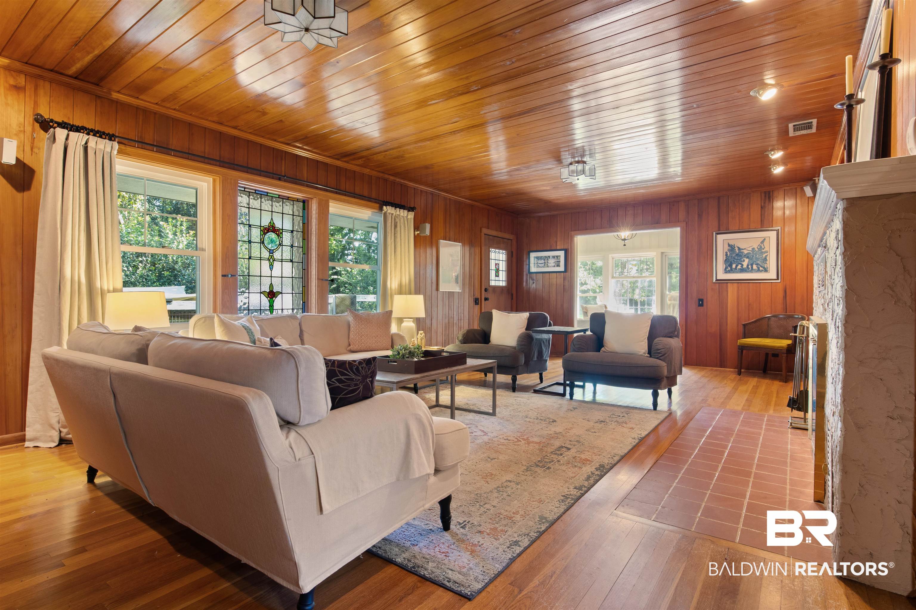 15100 Vasko Road Silverhill, AL 36576 - Photo 19 of 51 Living room with hardwood floors, wood walls, wooden ceiling, a premium fireplace and stain glassed feature window overlooking small porch and hydrangeas.