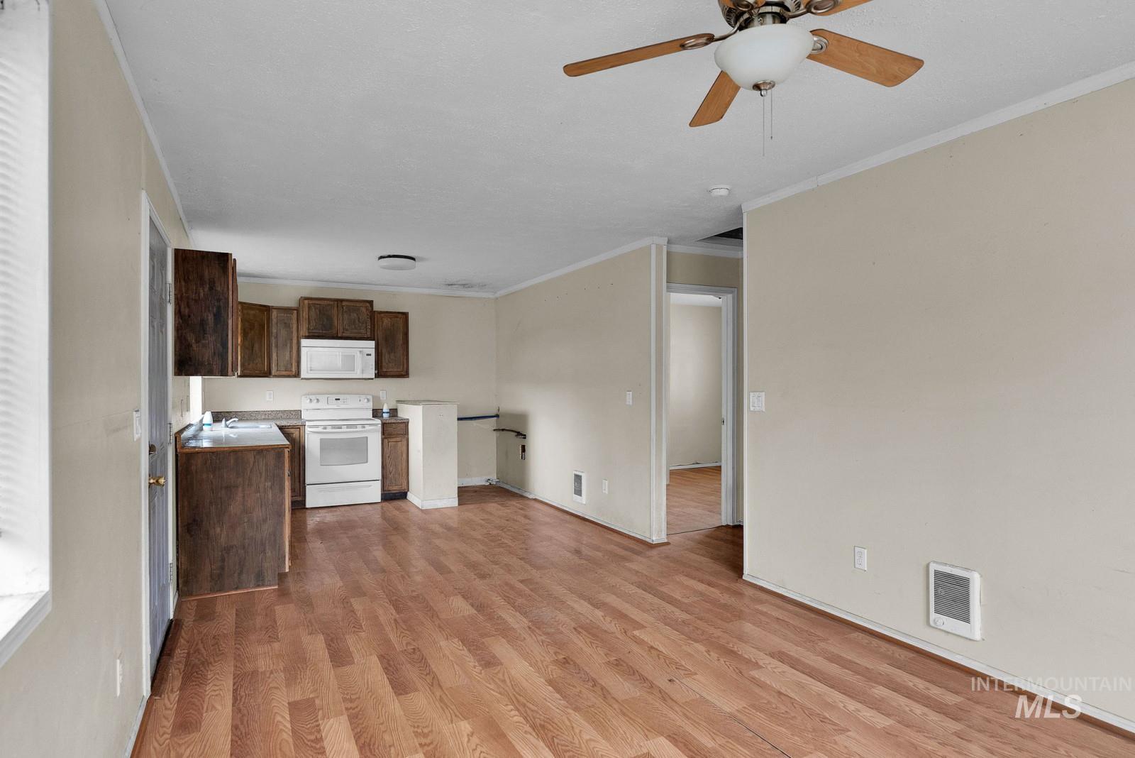 4715 West Reeves Street Coeur D'Alene, ID 83814 - Photo 11 of 24 Kitchen with white appliances, ornamental molding, light wood-type flooring, dark brown cabinetry, and light countertops