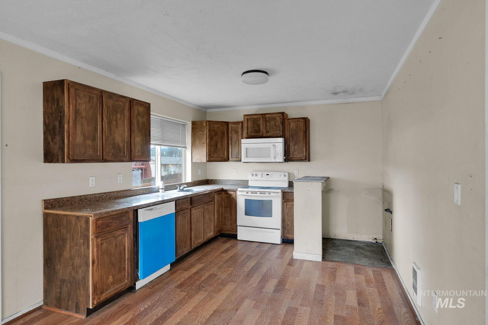4715 West Reeves Street Coeur D'Alene, ID 83814 - Photo 8 of 24 Kitchen featuring white appliances, ornamental molding, dark wood-type flooring, dark countertops, and dark brown cabinetry