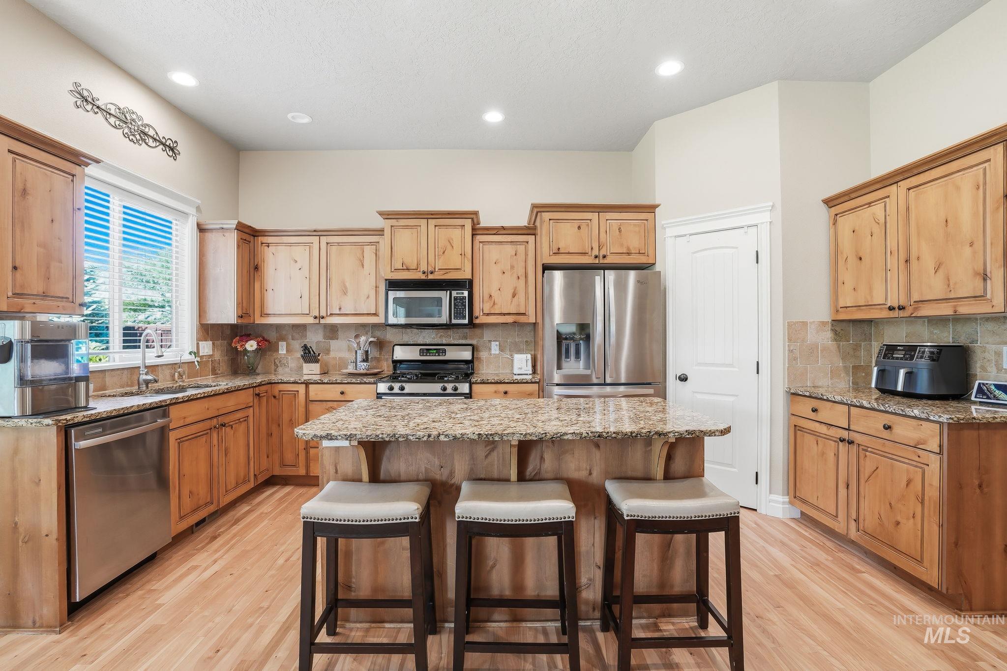 3969 North Hollymount Way Meridian, ID 83646 - Photo 9 of 47 Kitchen featuring wood-finish cabinetry, stainless steel appliances, a multi-tone granite countertop island, natural wood-finish flooring, and recessed lighting