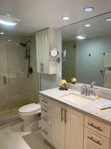 a bathroom with a granite countertop sink a toilet a mirror and shower
