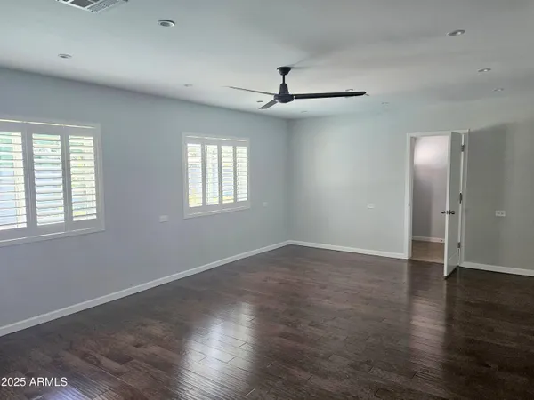 an empty room with wooden floor chandelier fan and windows