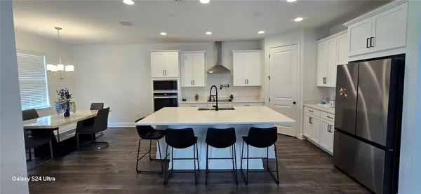 a kitchen with stainless steel appliances granite countertop a dining table chairs refrigerator and sink