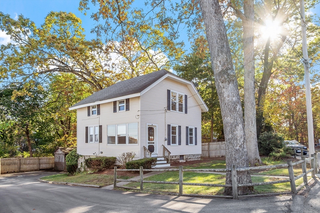 a view of a white house with a large tree and lawn chairs
