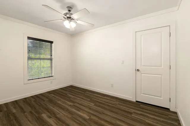 an empty room with wooden floor chandelier fan and windows