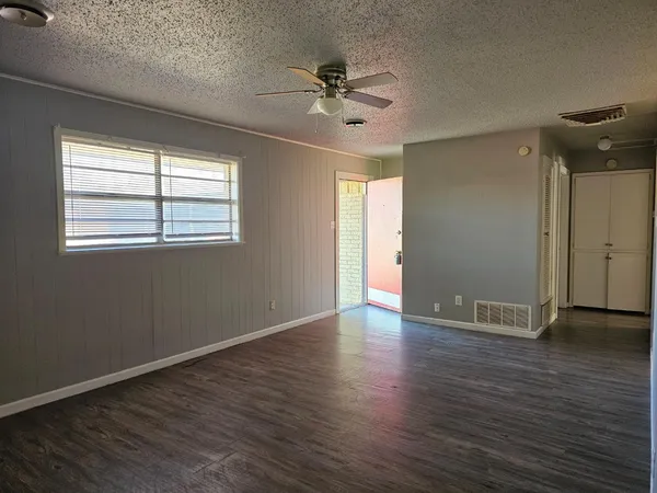 an empty room with wooden floor fan and windows