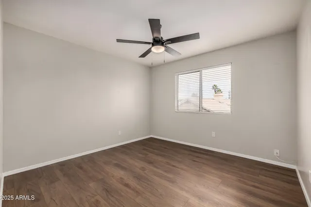 an empty room with wooden floor ceiling fan and windows