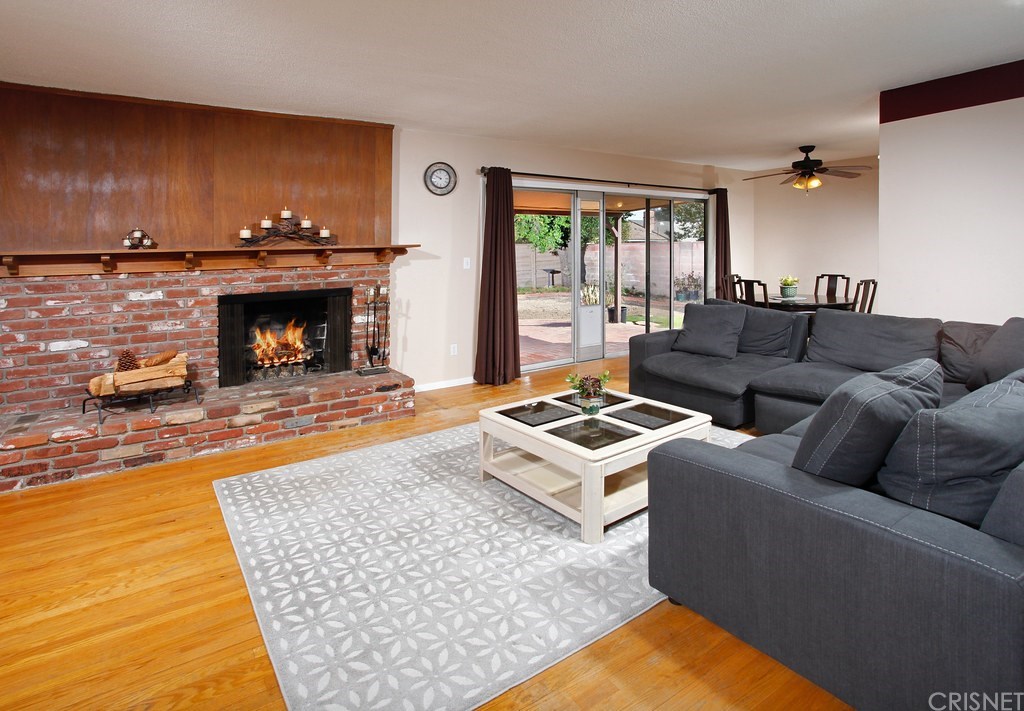 The living room is bathed in natural light from a multitude of windows and is complemented by a raised hearth brick fireplace with mantle and hardwood floors.