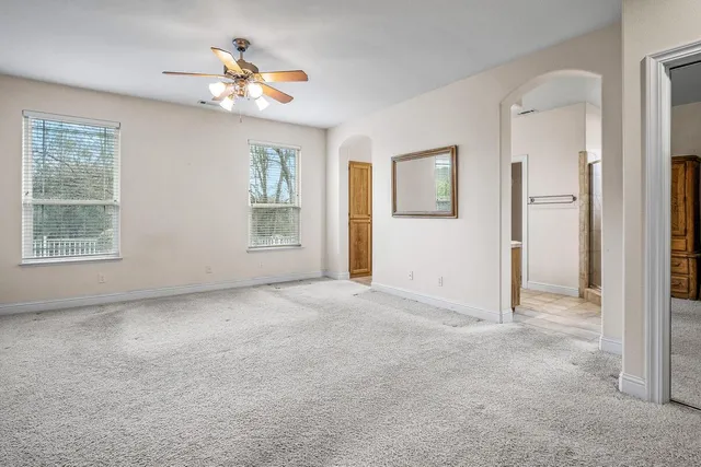 a view of an empty room with chandelier fan and windows