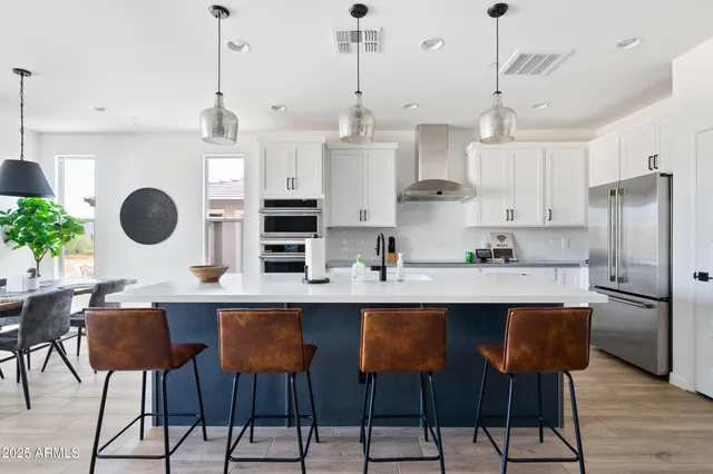 a kitchen with stainless steel appliances granite countertop a sink a stove a refrigerator and chairs with wooden floor