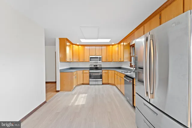 a kitchen with stainless steel appliances granite countertop a refrigerator a sink dishwasher a stove and white countertops with wooden floor