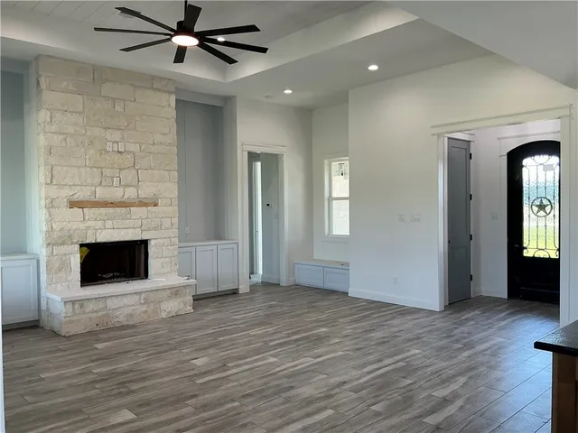 an empty room with wooden floor a ceiling fan a fireplace and windows