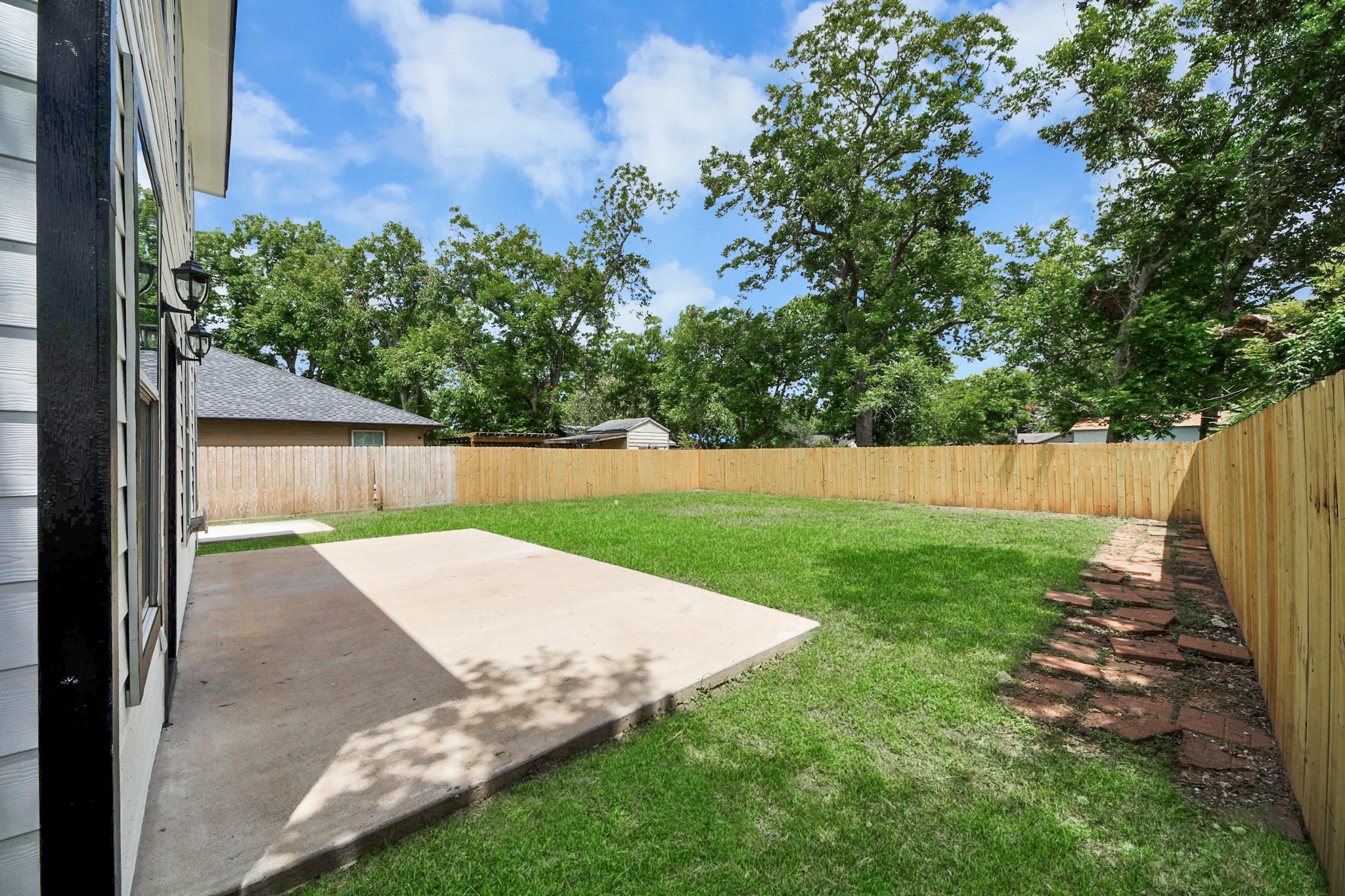 1105 East Kyle Road Clute, TX 77531 - Photo 38 of 44 Spacious backyard with two concrete patios, perfect for outdoor activities. The area is fenced for privacy and bordered by mature trees, offering a serene setting.