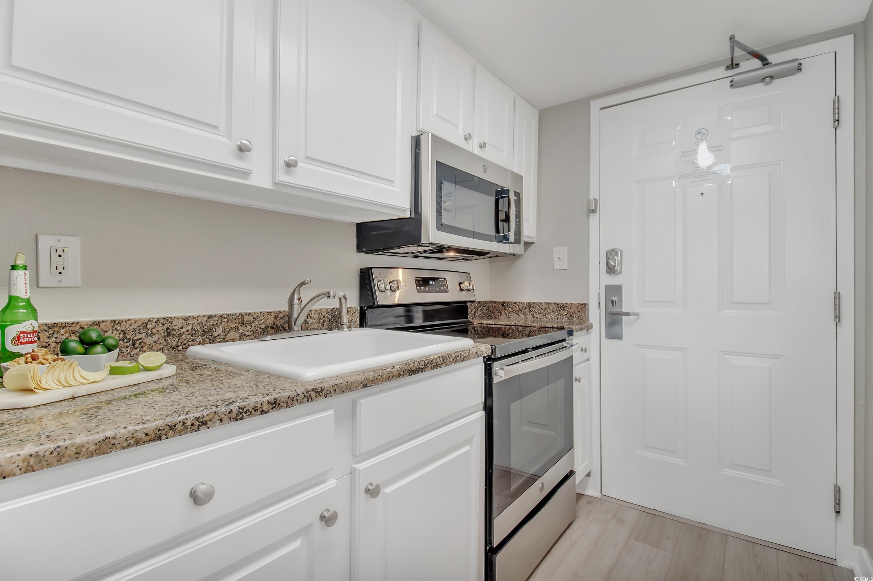 2710 North Ocean Boulevard, Unit 622 Myrtle Beach, SC 29577 - Photo 32 of 37 Kitchen featuring stainless steel appliances, white cabinetry, light wood-style floors, and dark stone counters