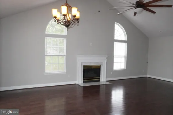 an empty room with wooden floor chandelier and windows