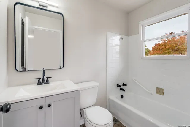 a bathroom with a toilet sink vanity tub and mirror