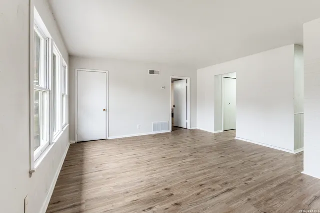 a view of an empty room with wooden floor and a window