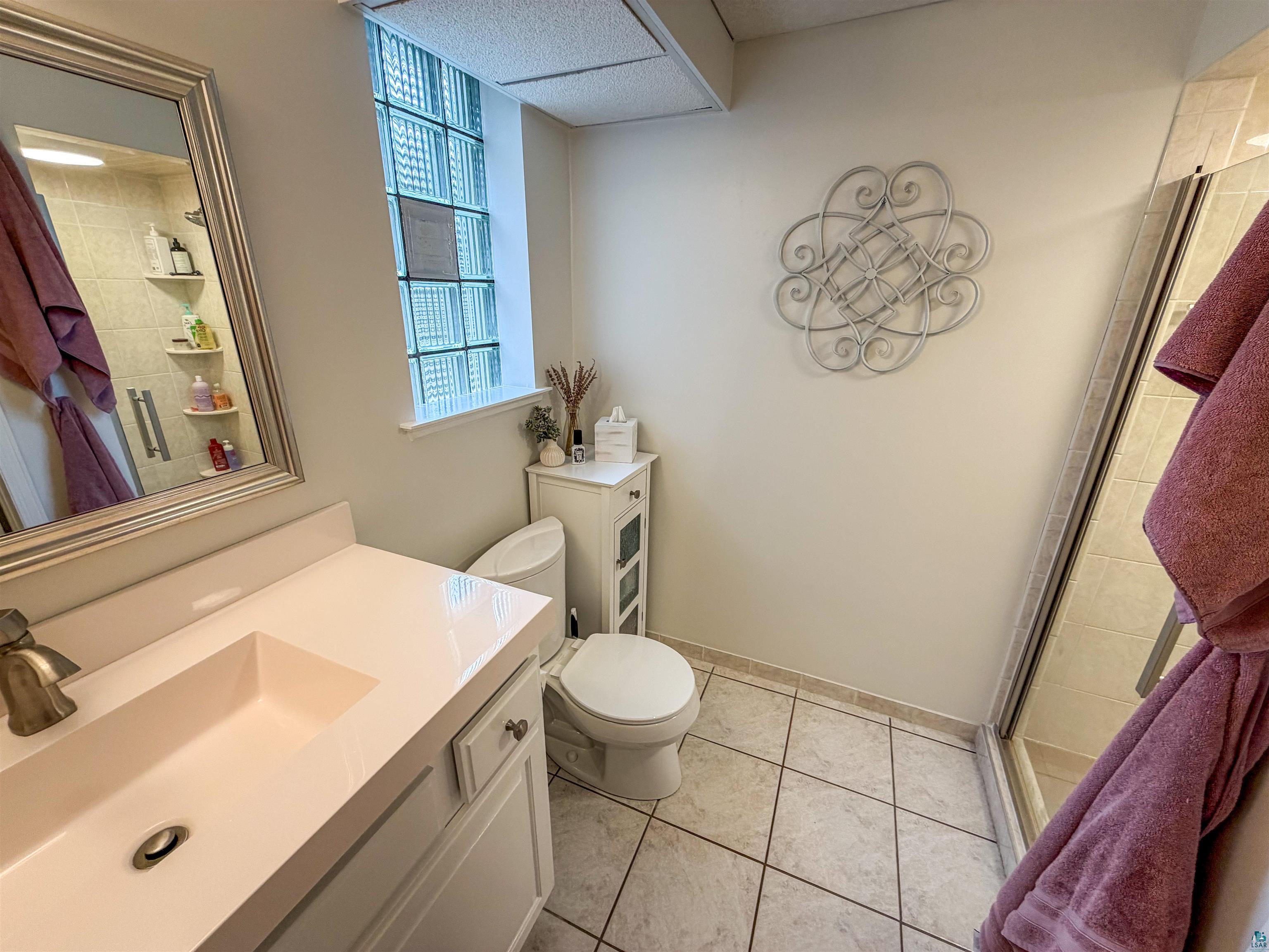 3704 Greysolon Road Duluth, MN 55804 - Photo 31 of 51 Bathroom featuring a built-in shower with glass enclosure, single vanity with integrated sink, tile flooring, and a glass block window