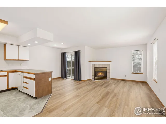a view of an empty room with wooden floor fireplace and a window