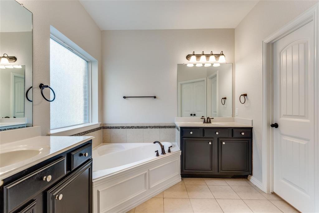 2344 Ranchview Drive Little Elm, TX 75068 - Photo 13 of 24 Bathroom featuring dual dark wood vanities with light countertops, a built-in corner soaking tub, a privacy window, and tile flooring