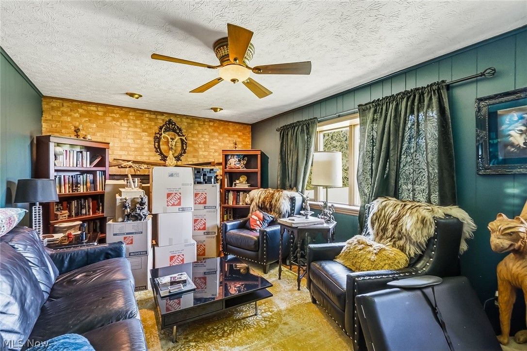 6890 Refugee Road Pickerington, OH 43147 - Photo 19 of 49 Cozy living area featuring a brick accent wall, wood-paneled walls, built-in shelving, and a ceiling fan with integrated lighting