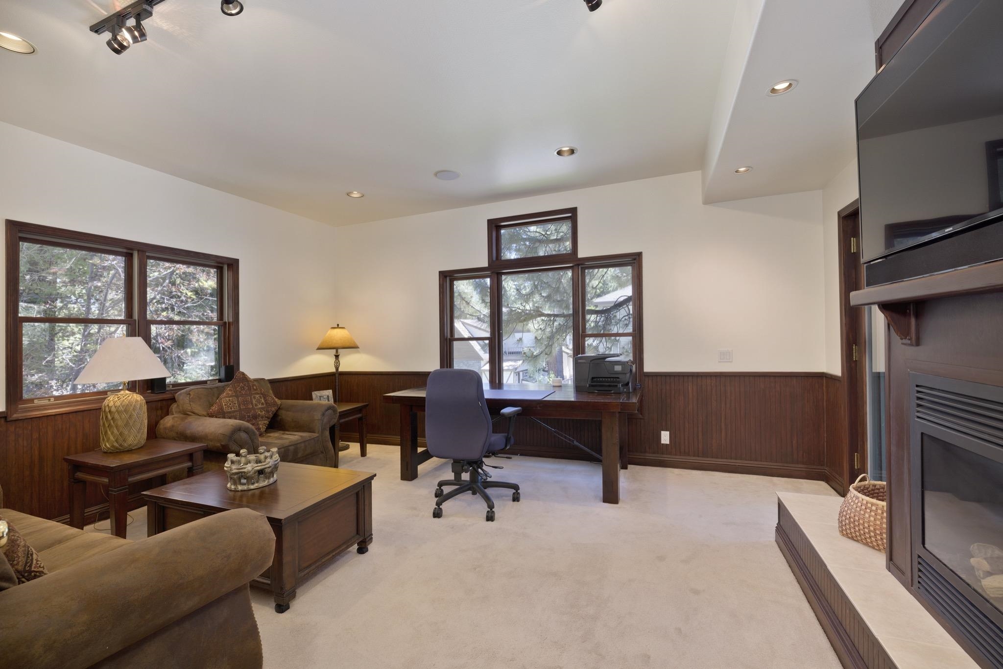 378 Ridge Way Mammoth Lakes, CA 93546 - Photo 19 of 43 Spacious room featuring a fireplace with a stone hearth, recessed lighting, track lighting, dark wood window frames, and wood paneling