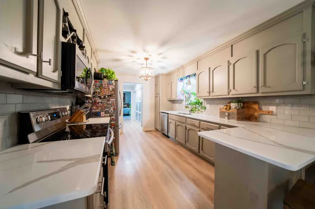 a kitchen with granite countertop a refrigerator a sink dishwasher and white cabinets with wooden floor