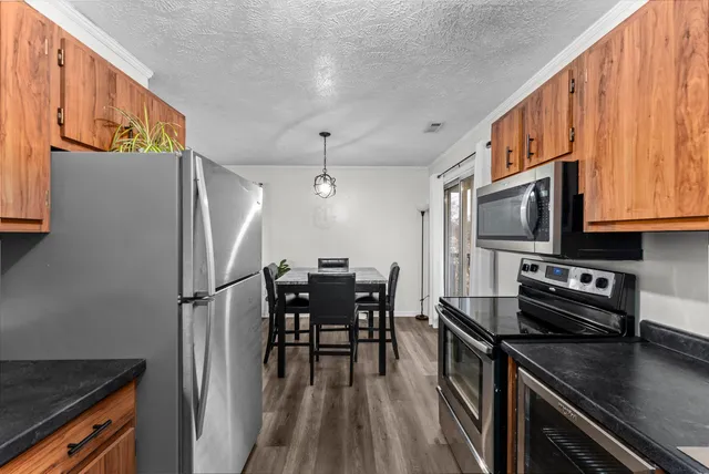 a kitchen with stainless steel appliances a refrigerator a stove a sink a dining table and chairs with wooden floor