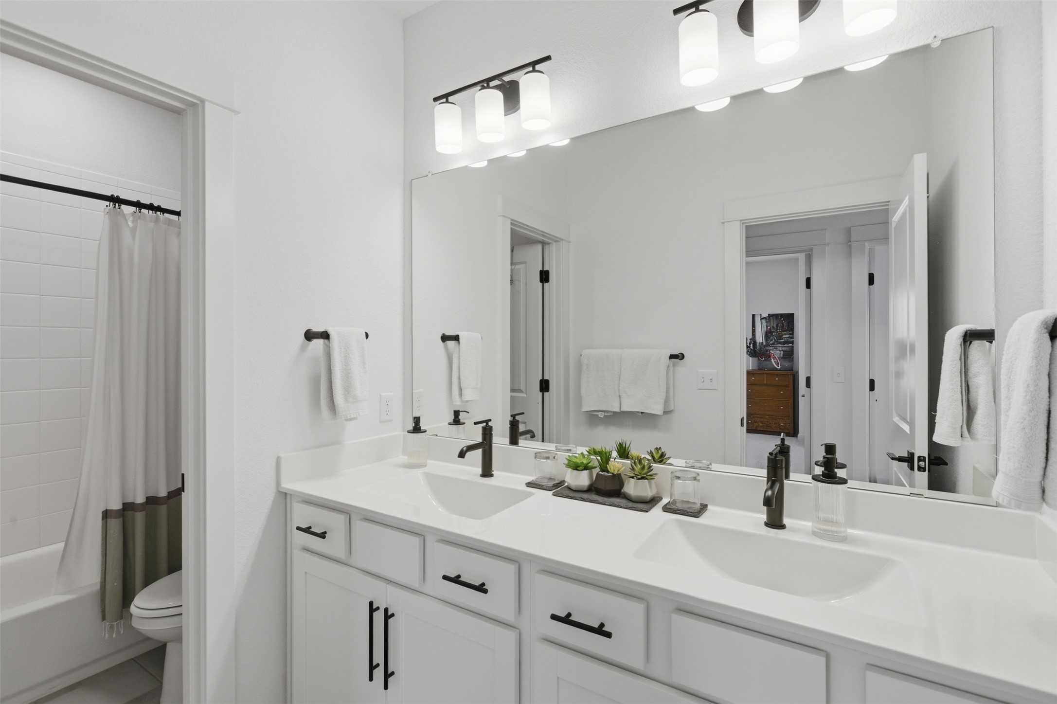 9001 Spire View Austin, TX 78744 - Photo 28 of 35 Double vanity featuring white cabinetry with black hardware, white countertops, dual undermount sinks with black faucets, and an expansive wall mirror