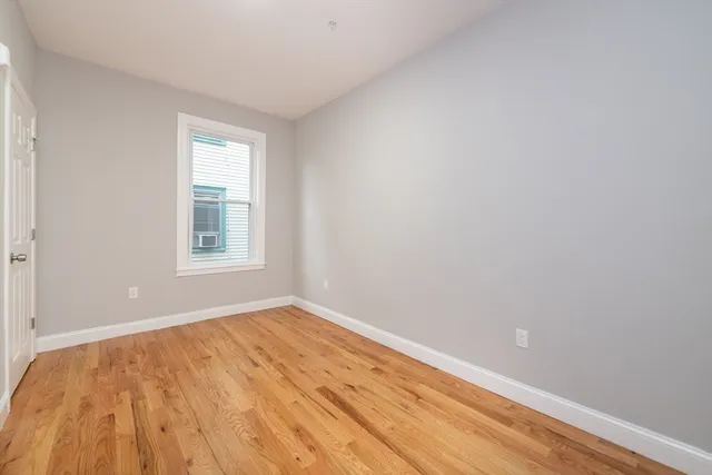 a view of an empty room with window and wooden floor