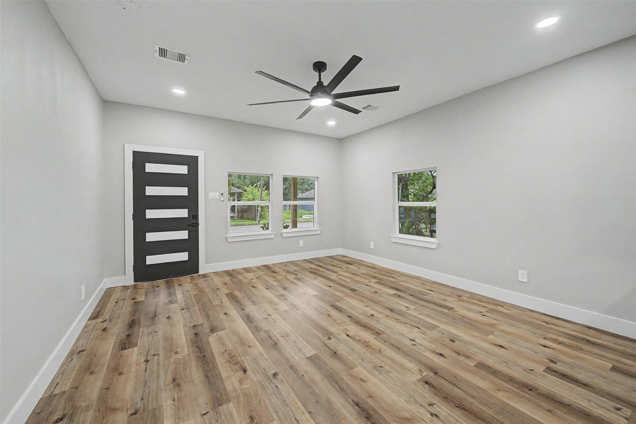 2338 Lidstone Street Houston, TX 77023 - Photo 10 of 17 This room features modern design with light gray walls, sleek luxury vinyl flooring, and a stylish black ceiling fan. Windows provide natural light, and a contemporary door adds a chic touch.