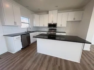a kitchen with granite countertop wooden floors a sink and white appliances