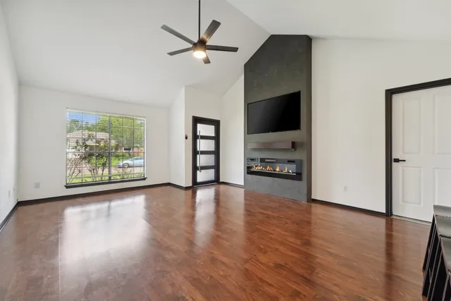 an empty room with wooden floor chandelier fan and windows