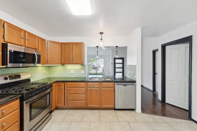 a kitchen with stainless steel appliances granite countertop a stove top oven a sink dishwasher and a refrigerator with wooden cabinets