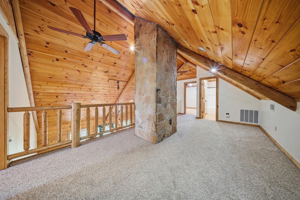 465 Emberson Ranch Road Pilot Point, TX 76258 - Photo 20 of 37 Loft area featuring sloped wood-paneled ceilings, wood railing, stone-clad pillar, and carpeted flooring