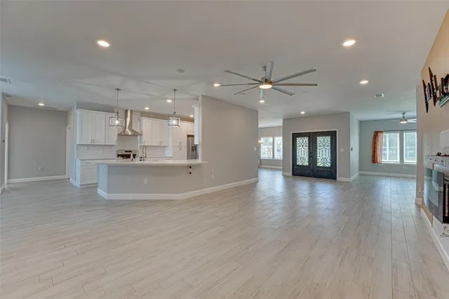 a view of an empty room and kitchen view with wooden floor