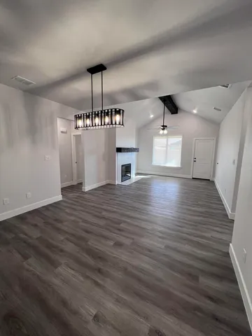 a view of an empty room with wooden floor and a kitchen